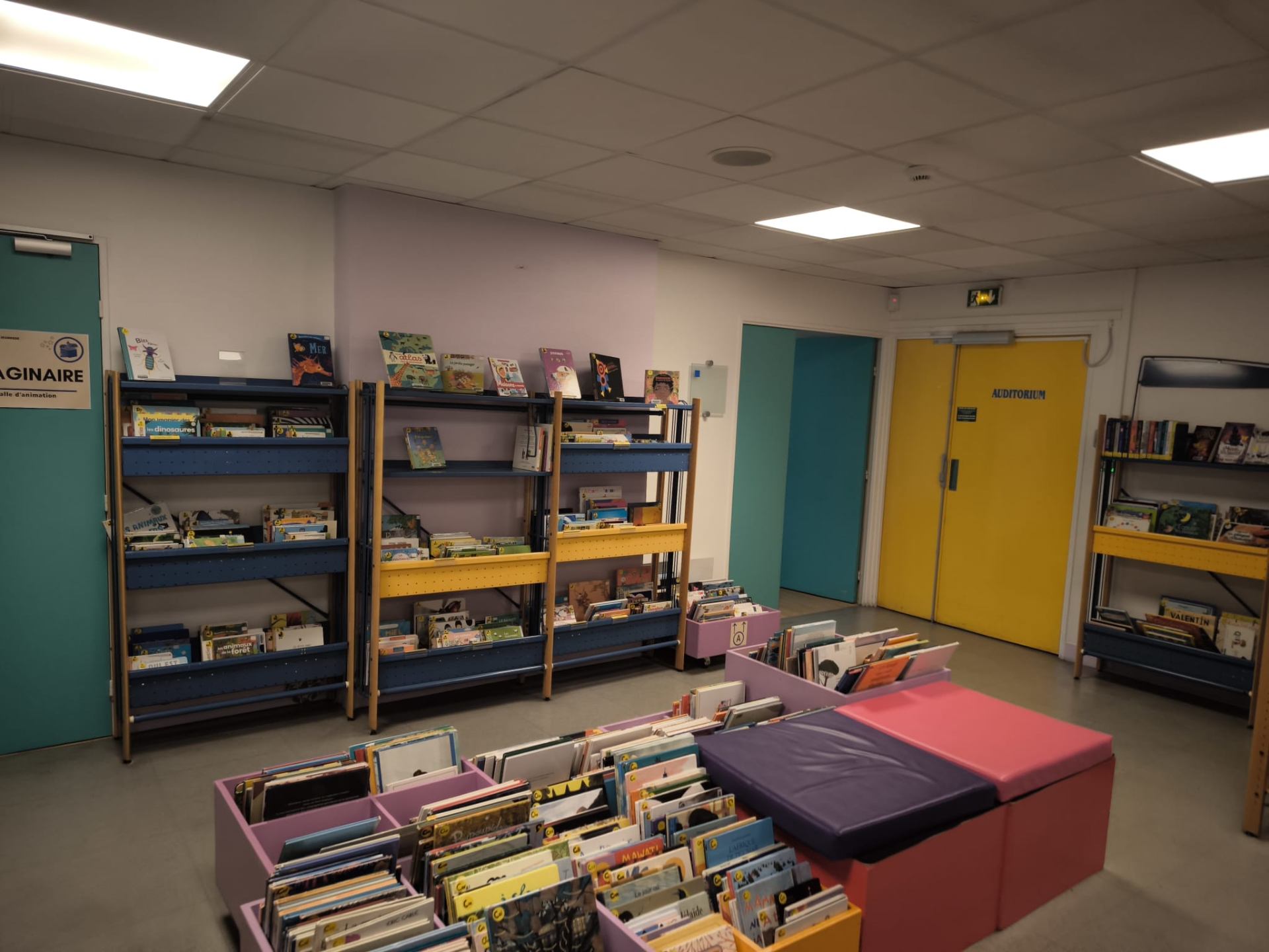 Espace jeunesse partenaire avec rayonnages de livres et coussins de lecture